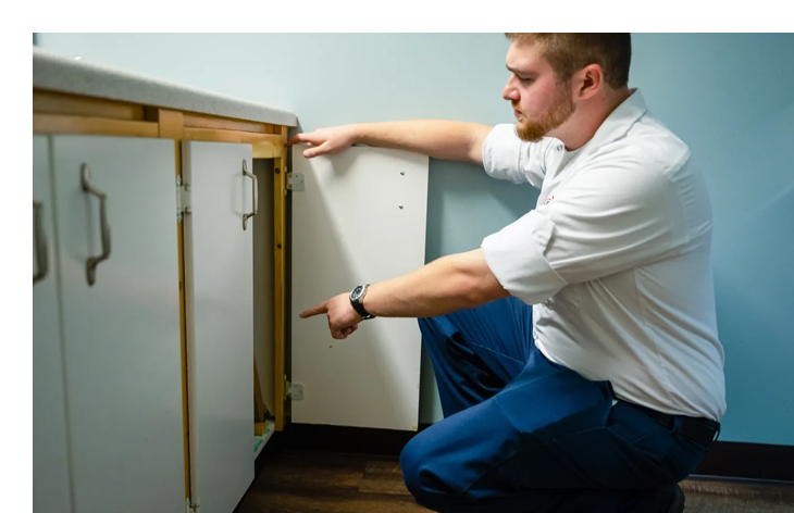 A man kneeling down in front of a cabinet.