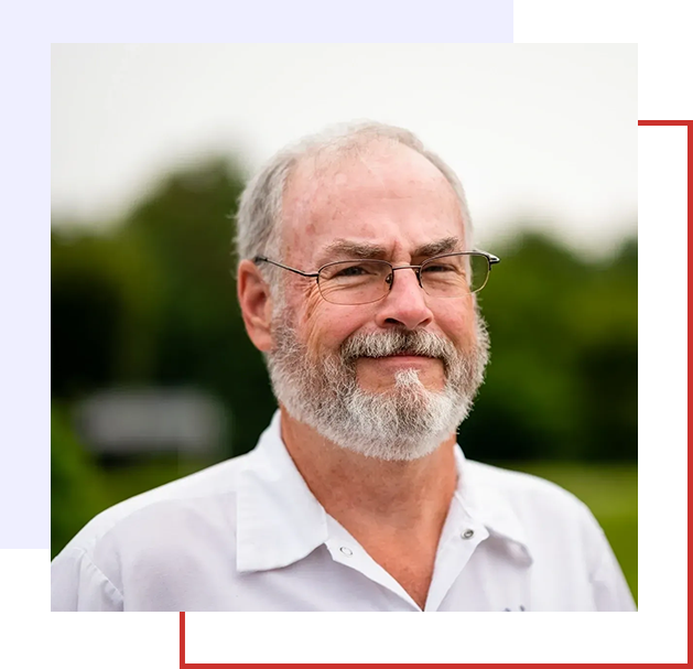 A man with white beard and glasses in front of trees.